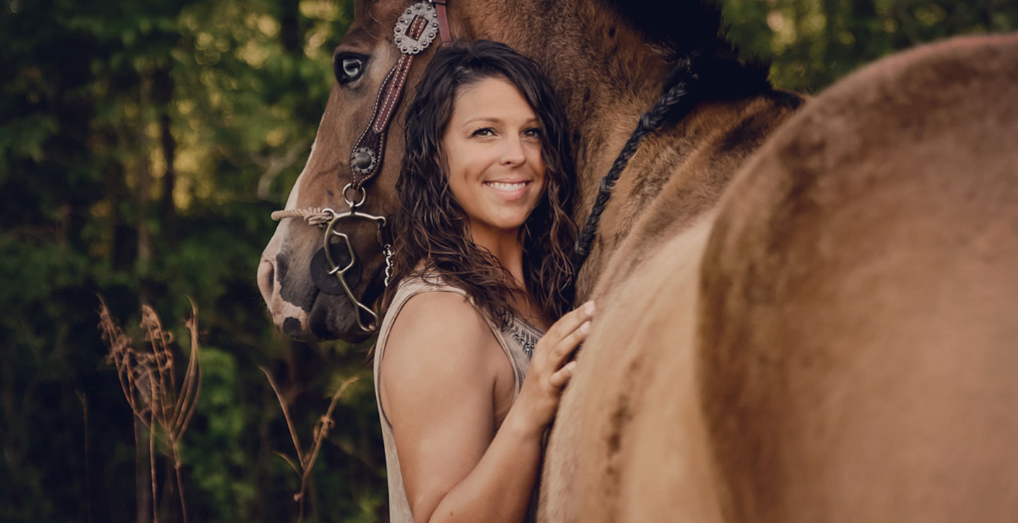 Horse trainer, Taylor Rae Vaughn, posing next to and hugging her tan horse. 